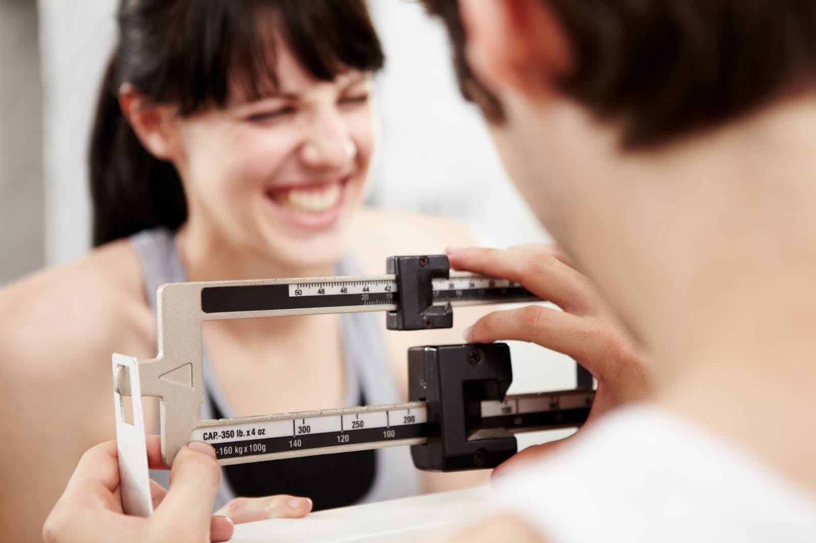 A woman smiles while a male doctor weighs her after receiving semaglutide near Lakeville, MN